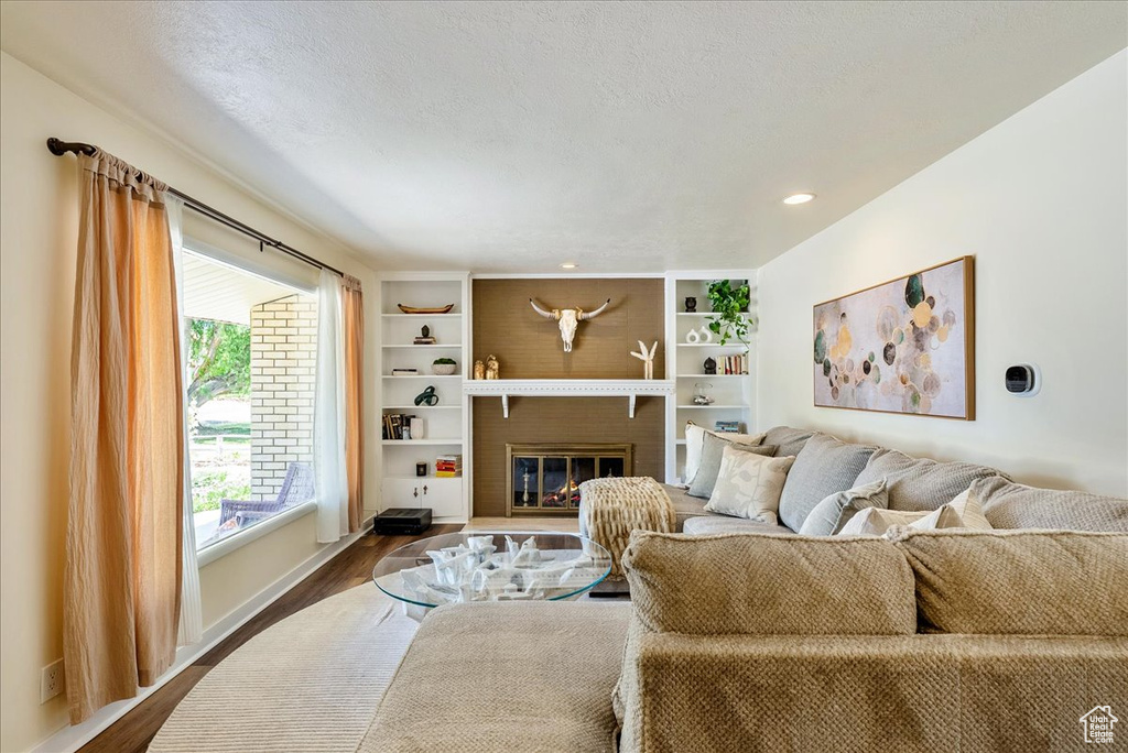 Living room featuring dark wood-style floors, a brick fireplace, a textured ceiling, and recessed lighting