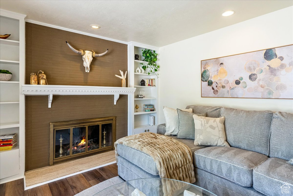 Living area featuring wood finished floors, a glass covered fireplace, recessed lighting, and built in shelves