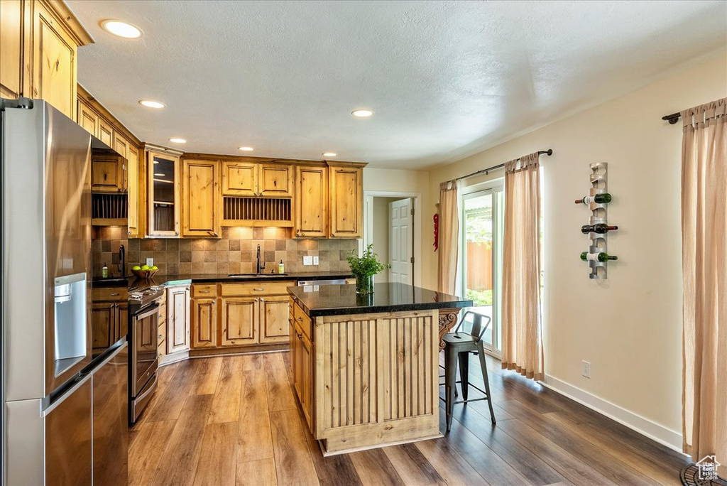 Kitchen featuring appliances with stainless steel finishes, dark countertops, dark wood-style floors, a kitchen island, and recessed lighting