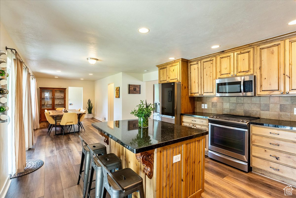 Kitchen with stainless steel appliances, a kitchen breakfast bar, dark wood-type flooring, a center island, and recessed lighting
