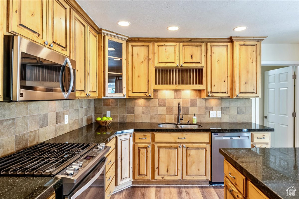 Kitchen with stainless steel appliances, dark stone countertops, glass insert cabinets, light wood-style floors, and recessed lighting