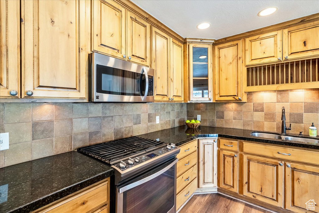 Kitchen with appliances with stainless steel finishes, dark stone counters, backsplash, light wood finished floors, and glass insert cabinets