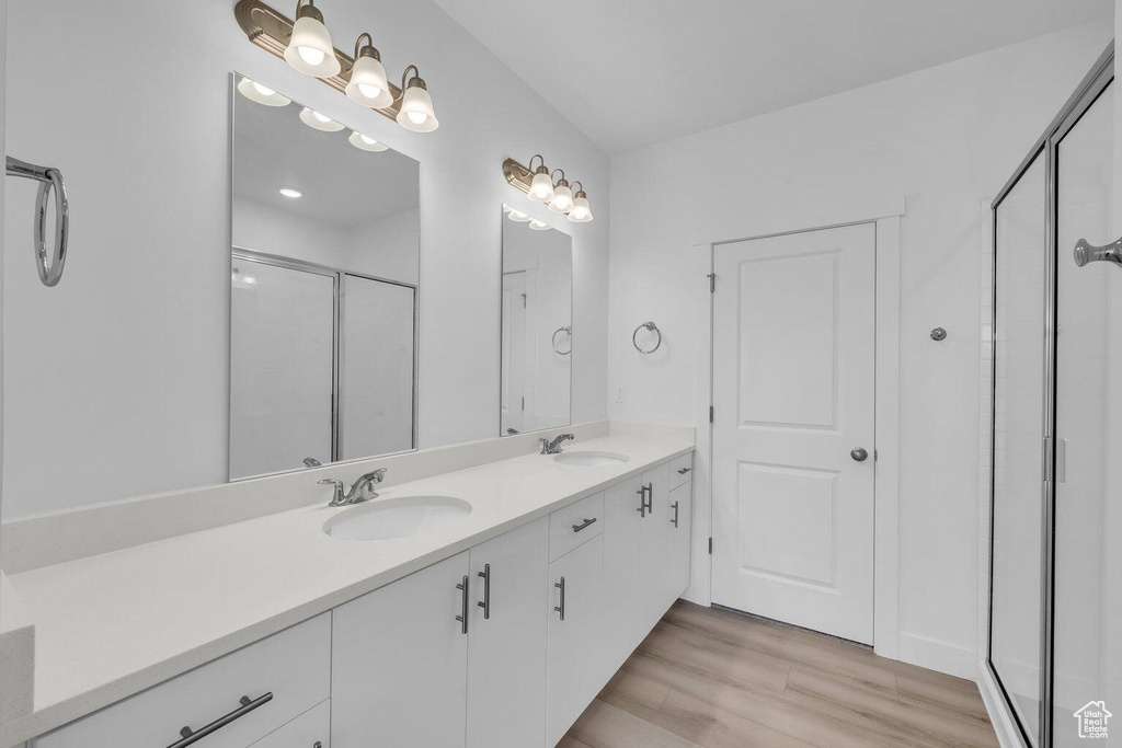 Bathroom featuring a shower stall, double vanity, and wood finished floors