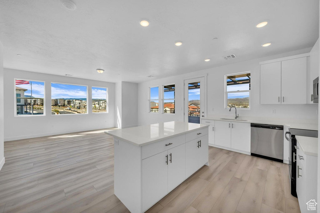 Kitchen with stainless steel dishwasher, recessed lighting, a center island, light wood-style floors, and light countertops