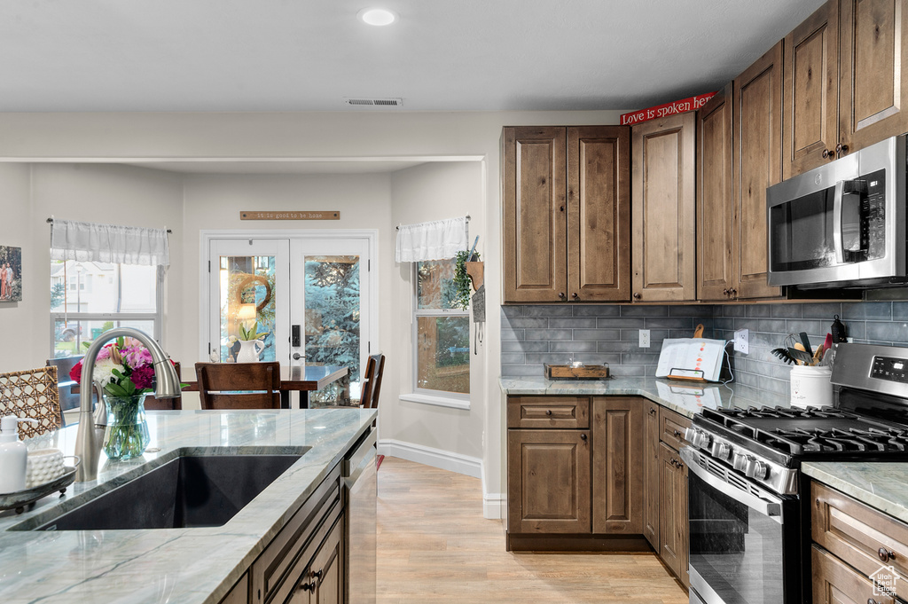 Kitchen with stainless steel appliances, light stone countertops, decorative backsplash, light wood-style floors, and recessed lighting