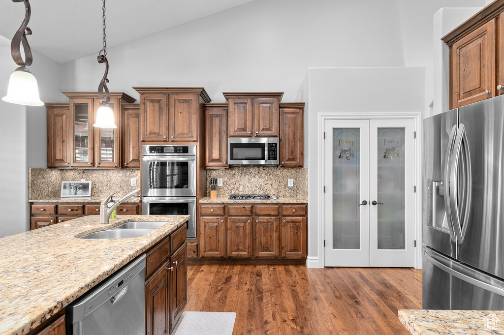 Kitchen with stainless steel appliances, pendant lighting, backsplash, light stone counters, and high vaulted ceiling