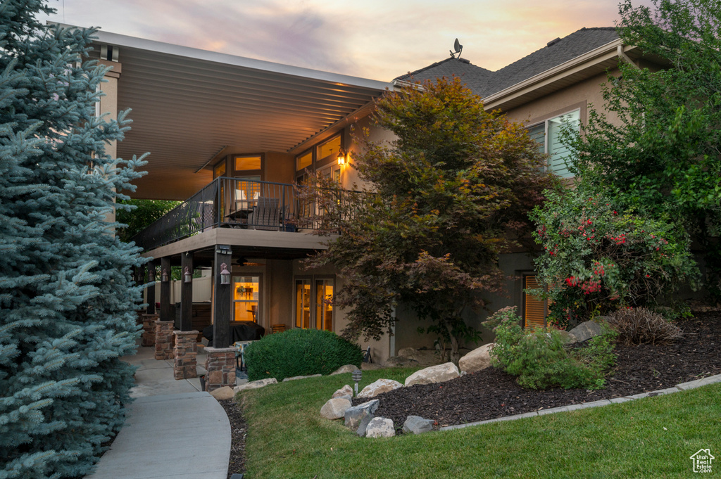 Back of house at dusk featuring a balcony and stucco siding