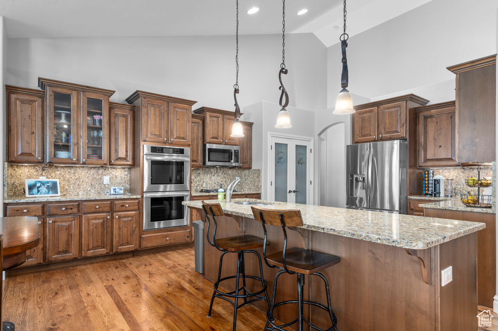 Kitchen featuring appliances with stainless steel finishes, high vaulted ceiling, backsplash, light stone countertops, and a kitchen bar