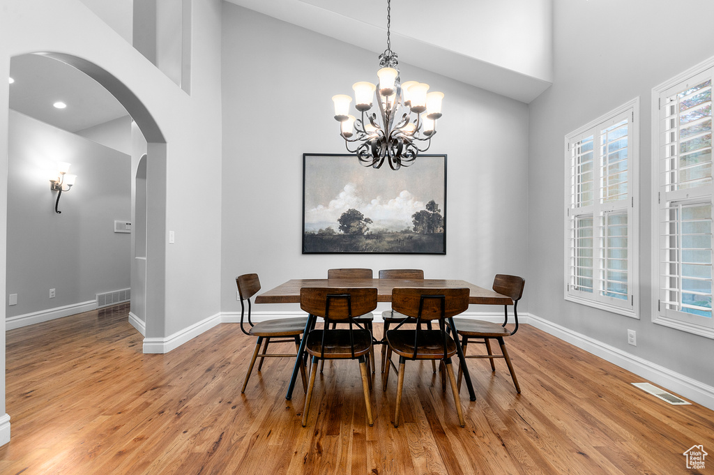 Dining space featuring arched walkways, high vaulted ceiling, light wood-style floors, a chandelier, and plenty of natural light