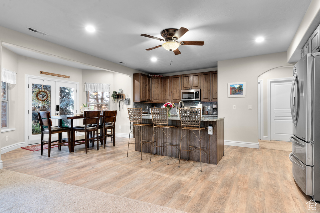 Kitchen featuring appliances with stainless steel finishes, a ceiling fan, light wood-type flooring, a breakfast bar, and backsplash