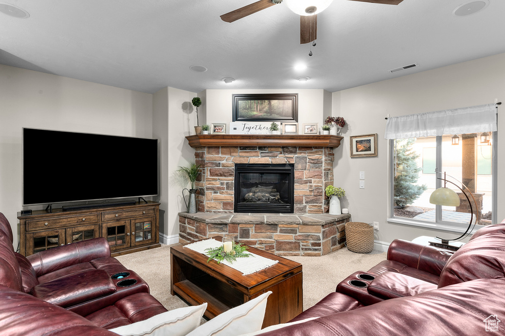 Carpeted living area featuring a ceiling fan and a stone fireplace
