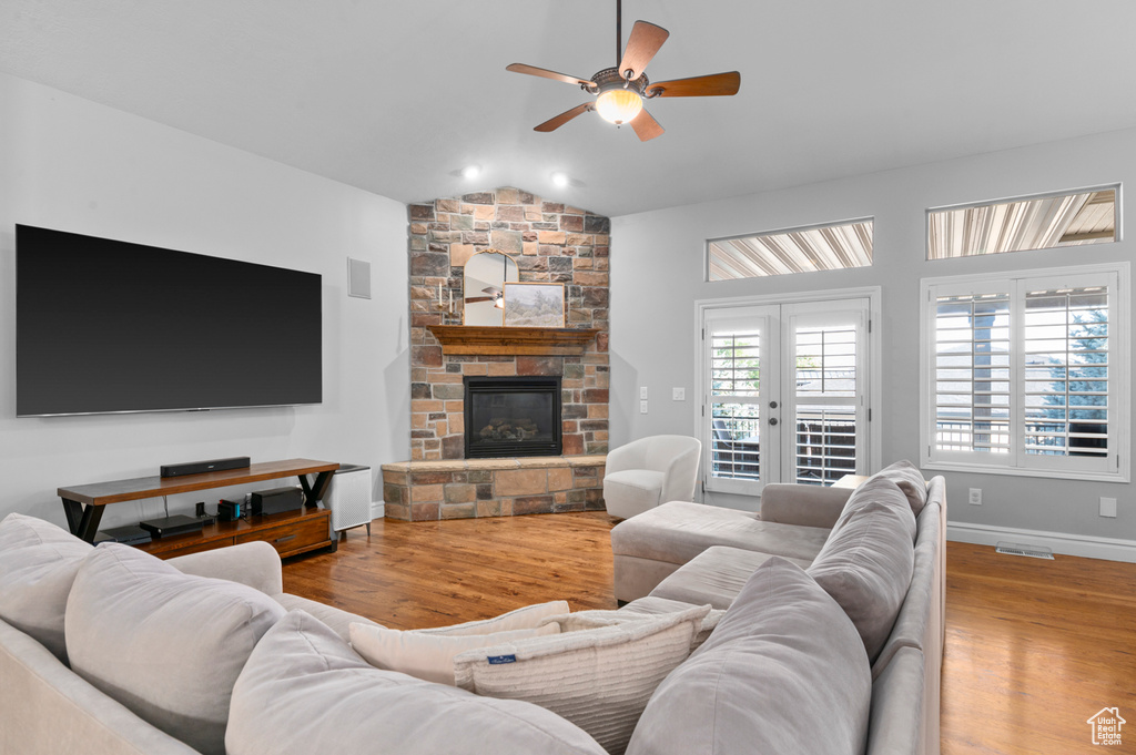 Living area with a ceiling fan, vaulted ceiling, wood finished floors, and a fireplace