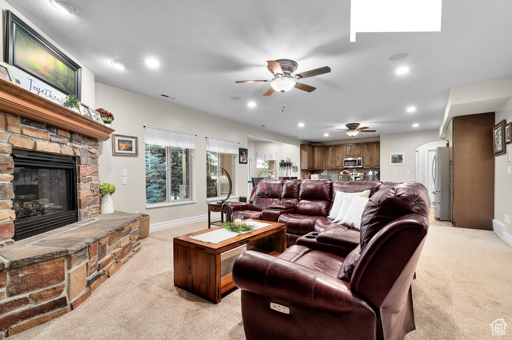 Living room featuring light colored carpet, a ceiling fan, a fireplace, recessed lighting, and arched walkways