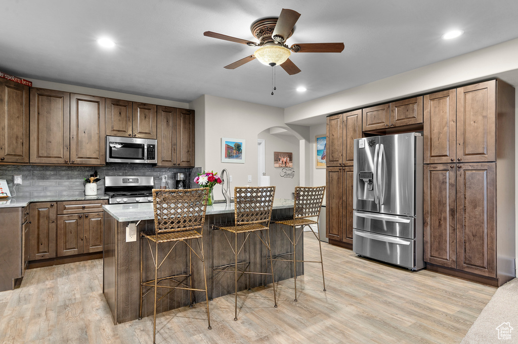 Kitchen with stainless steel appliances, a ceiling fan, arched walkways, a kitchen bar, and backsplash