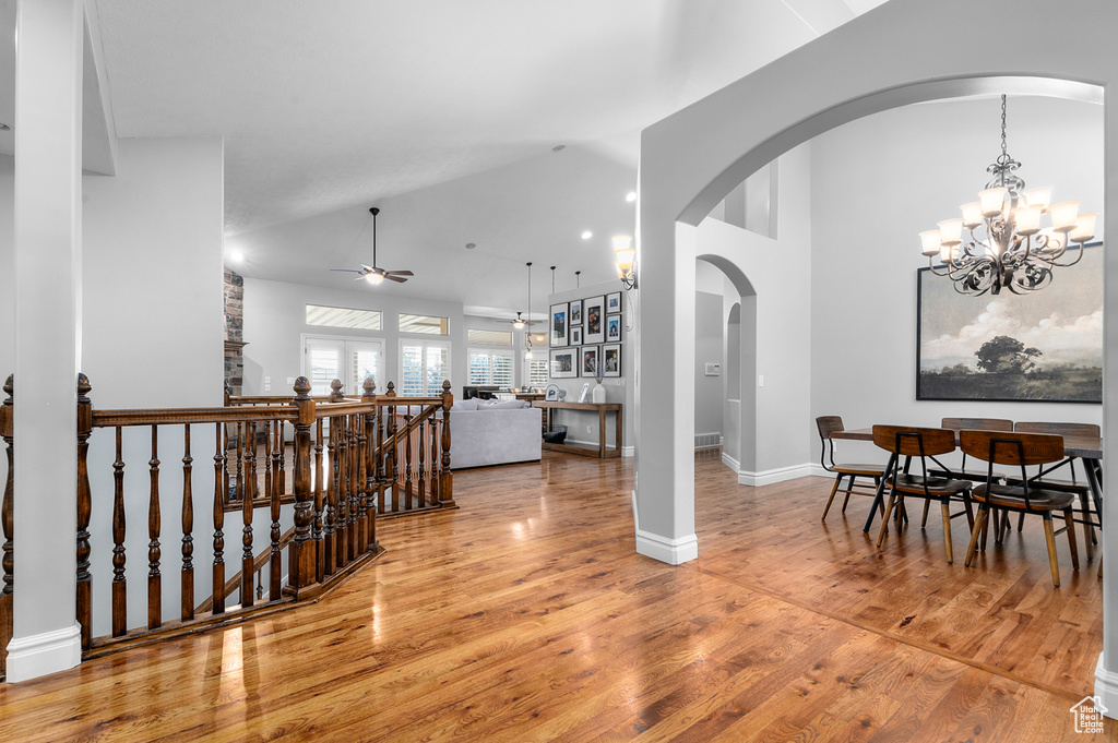 Corridor with an upstairs landing, high vaulted ceiling, wood finished floors, a chandelier, and arched walkways