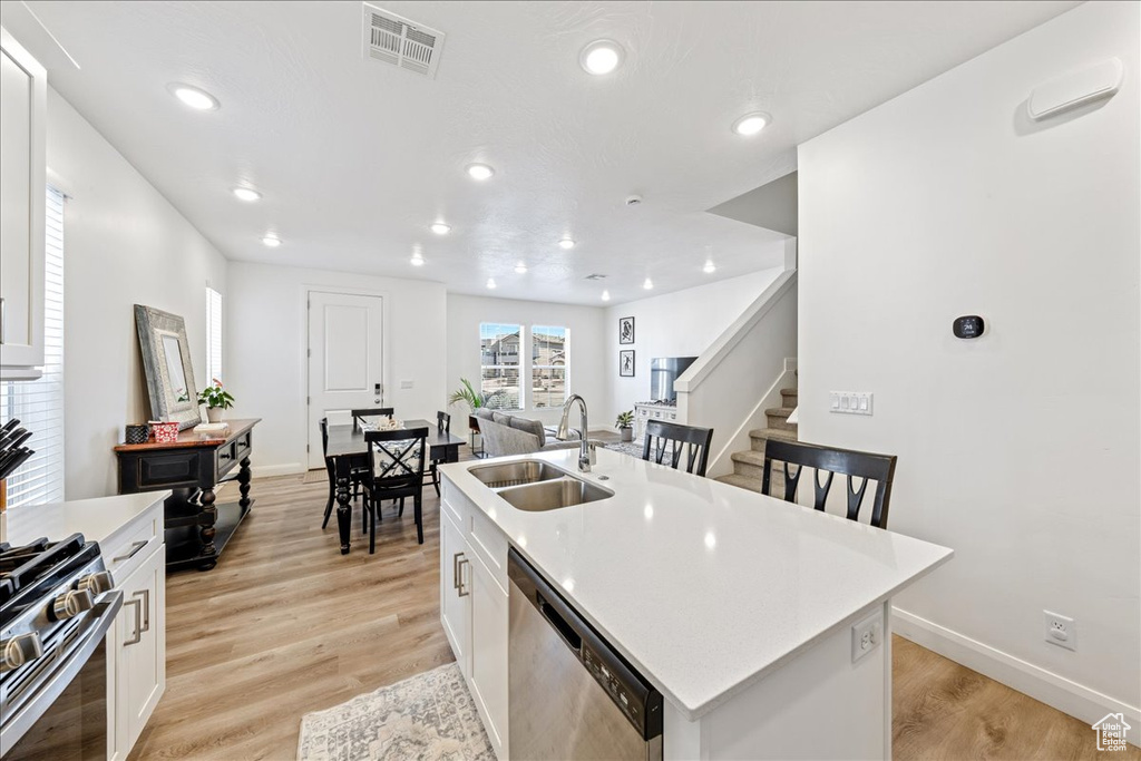 Kitchen with appliances with stainless steel finishes, white cabinetry, a kitchen island with sink, light countertops, and recessed lighting