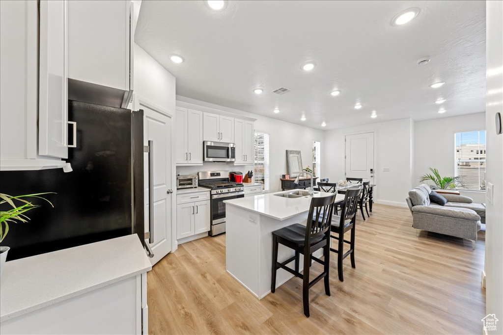 Kitchen featuring appliances with stainless steel finishes, a breakfast bar area, white cabinets, light wood-style floors, and recessed lighting