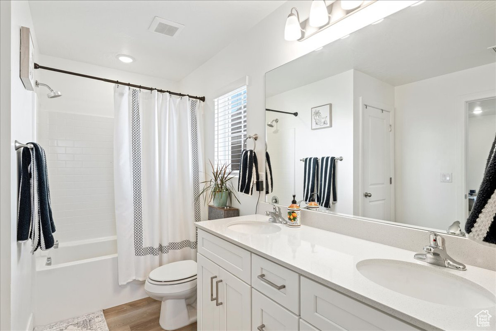 Bathroom featuring wood finished floors, double vanity, and shower / bath combo