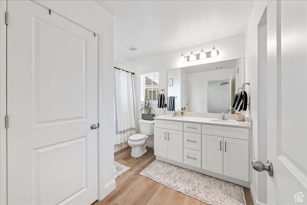Bathroom with double vanity, wood finished floors, and a shower with shower curtain