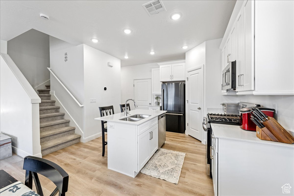 Kitchen with appliances with stainless steel finishes, a kitchen breakfast bar, white cabinetry, light wood finished floors, and light countertops