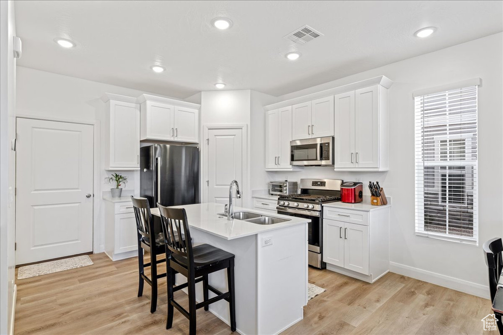 Kitchen with appliances with stainless steel finishes, a kitchen bar, white cabinetry, light countertops, and recessed lighting