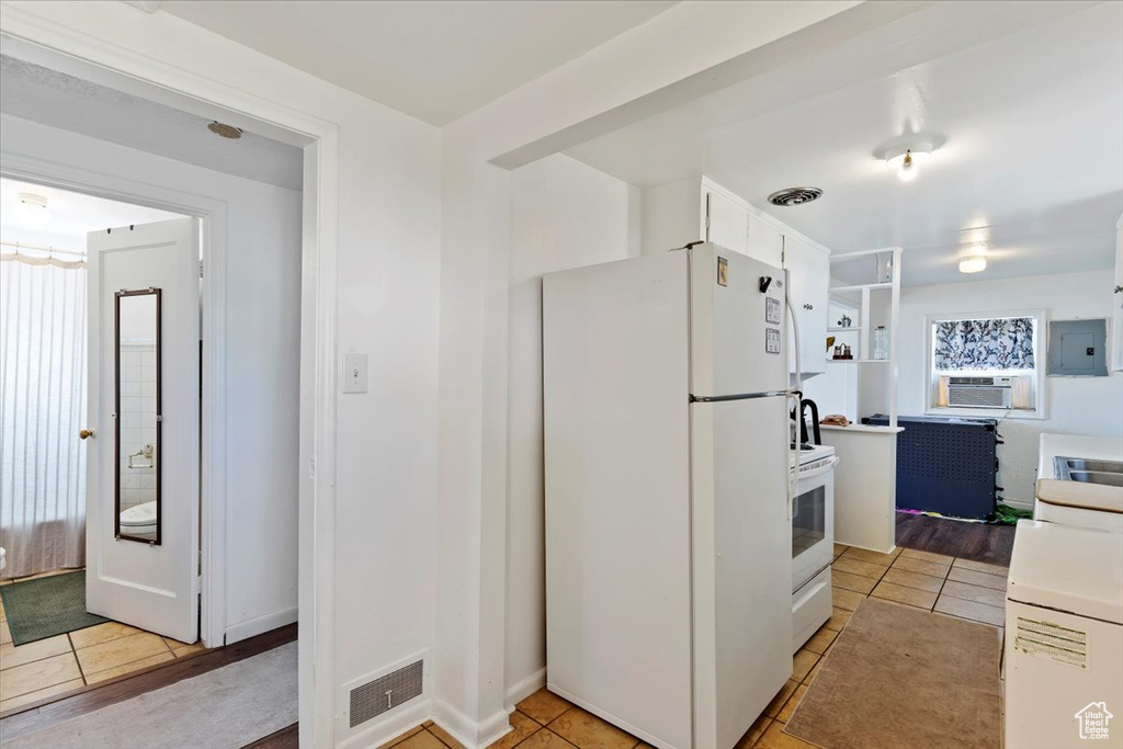 Kitchen featuring white appliances, electric panel, cooling unit, light tile patterned floors, and light countertops