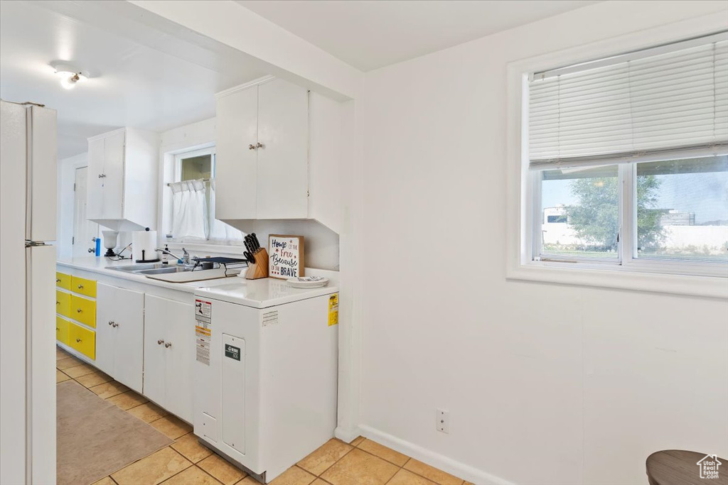 Kitchen featuring freestanding refrigerator, light tile patterned floors, white cabinets, and light countertops
