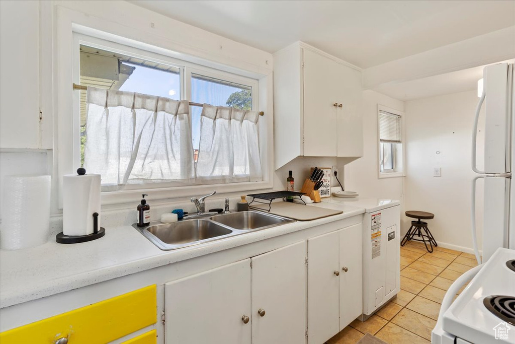 Kitchen featuring freestanding refrigerator, white cabinets, light tile patterned floors, and range