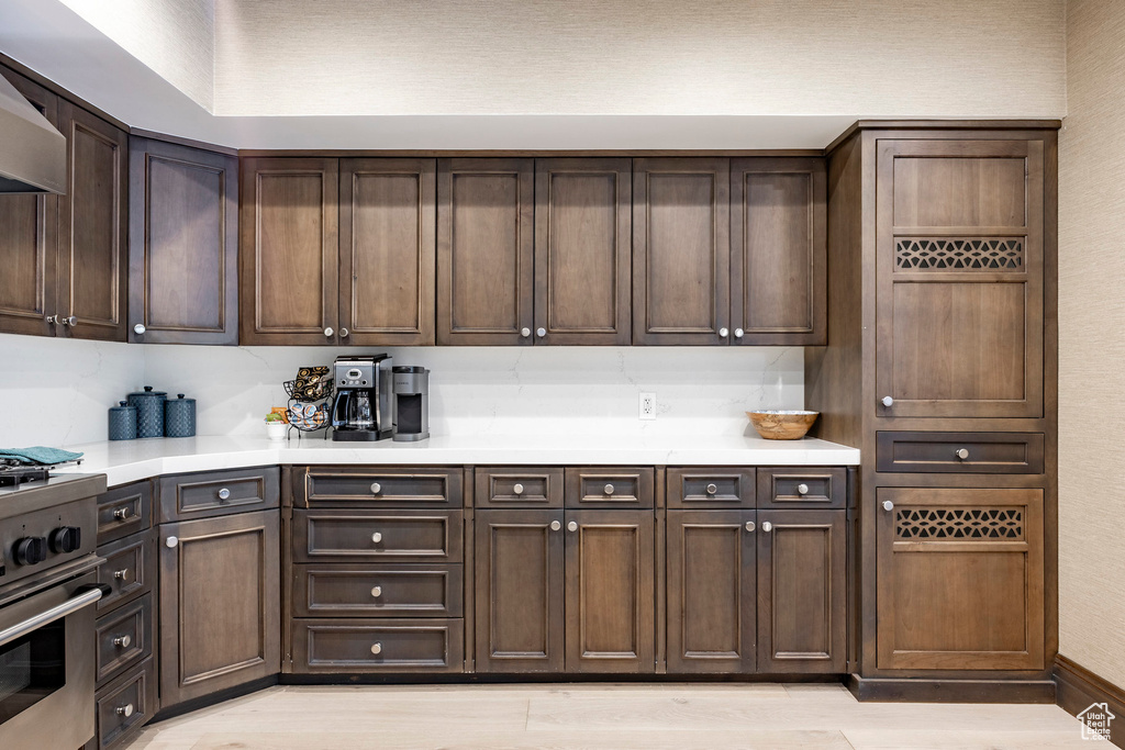 Kitchen with gas range, light countertops, range hood, and light wood-style floors