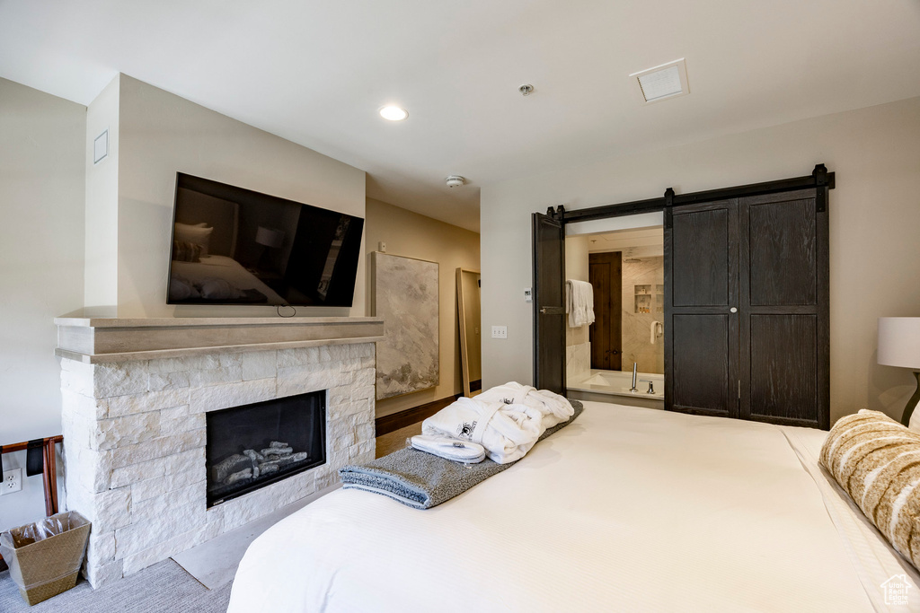 Bedroom featuring carpet floors, a stone fireplace, a barn door, and connected bathroom