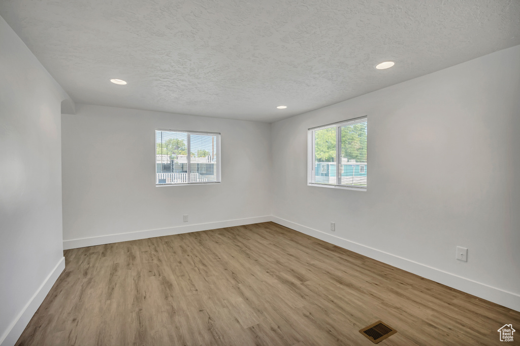 Spare room featuring healthy amount of natural light, wood finished floors, a textured ceiling, and recessed lighting