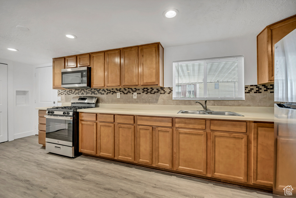 Kitchen with stainless steel appliances, brown cabinetry, light countertops, light wood finished floors, and backsplash