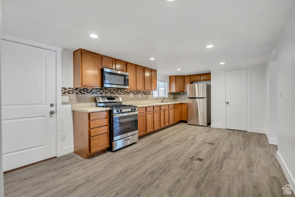 Kitchen with stainless steel appliances, light wood-style floors, light countertops, decorative backsplash, and recessed lighting
