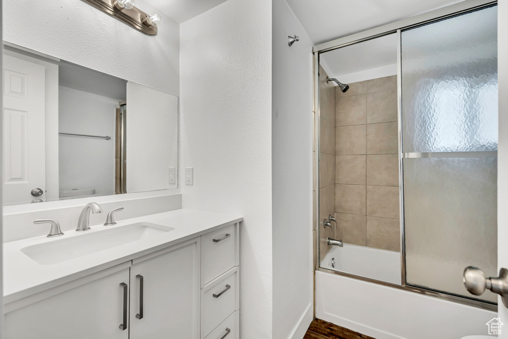 Full bath with vanity, bath / shower combo with glass door, and wood finished floors