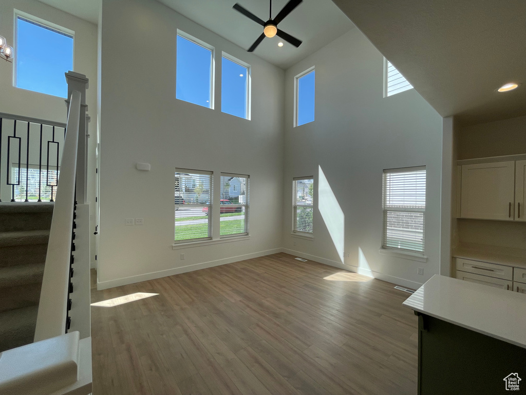 Unfurnished living room with wood finished floors, stairs, ceiling fan, a high ceiling, and plenty of natural light