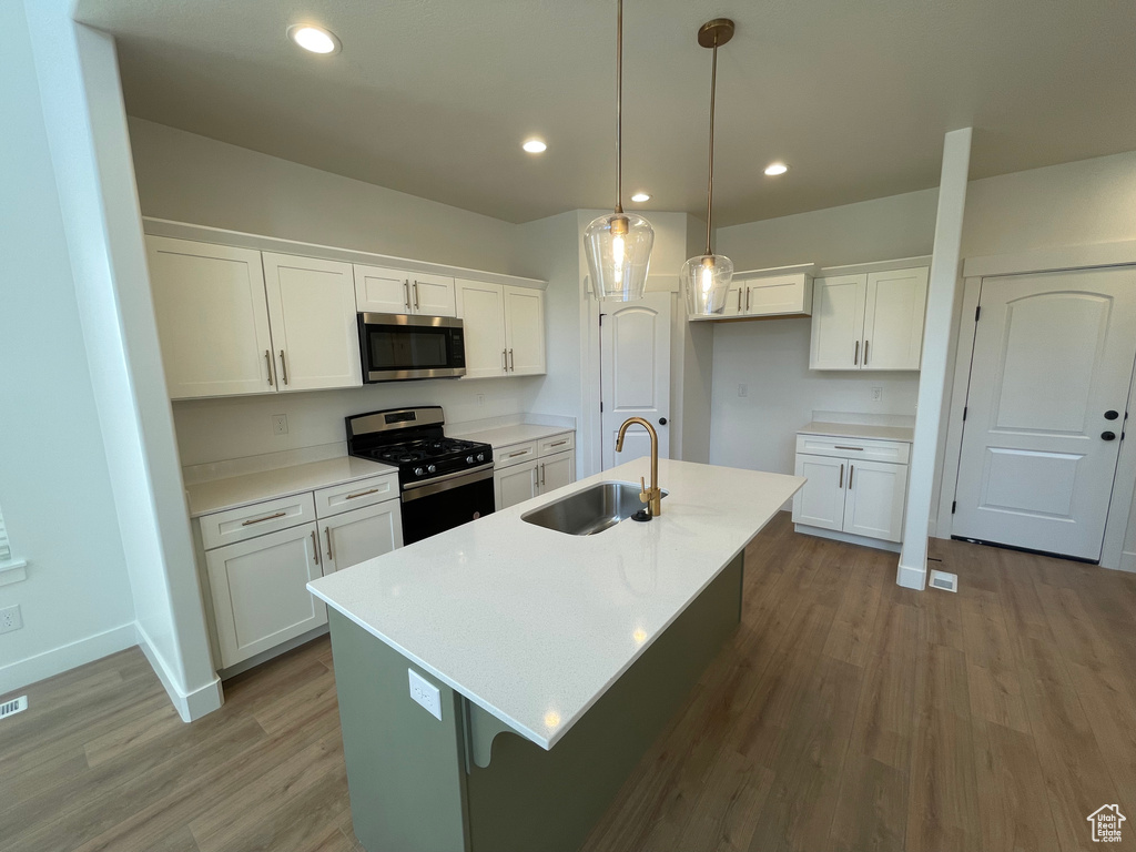 Kitchen featuring stainless steel appliances, wood finished floors, white cabinetry, light countertops, and recessed lighting