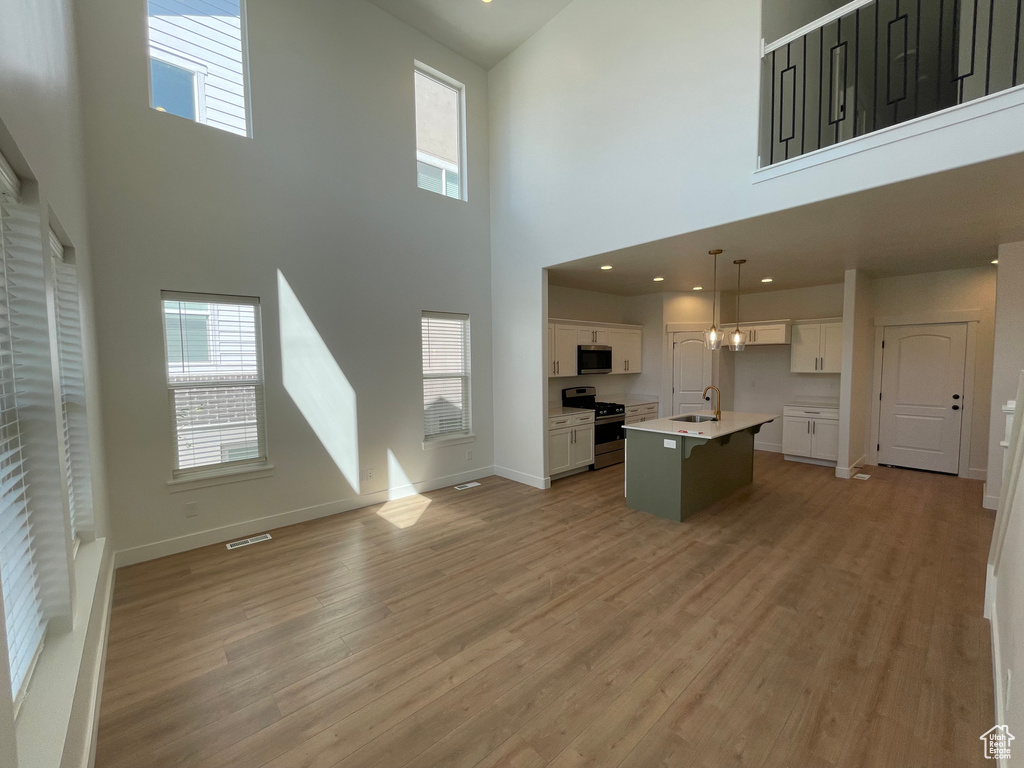 Kitchen featuring appliances with stainless steel finishes, open floor plan, white cabinetry, a towering ceiling, and light wood-type flooring