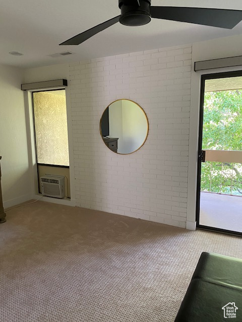 Spare room with carpet floors, a ceiling fan, brick wall, and an AC wall unit