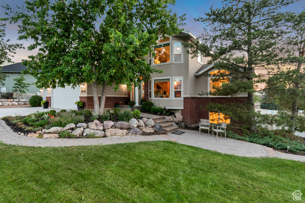 View of front of property featuring brick siding, a yard, stucco siding, a garage, and driveway
