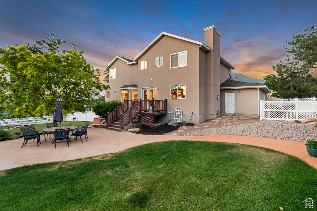 Rear view of house featuring a patio, a wooden deck, a chimney, and stucco siding