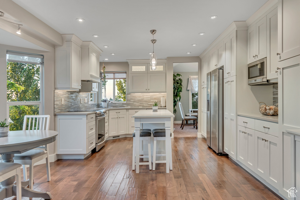 Kitchen featuring stainless steel appliances, a center island, light countertops, decorative backsplash, and white cabinets