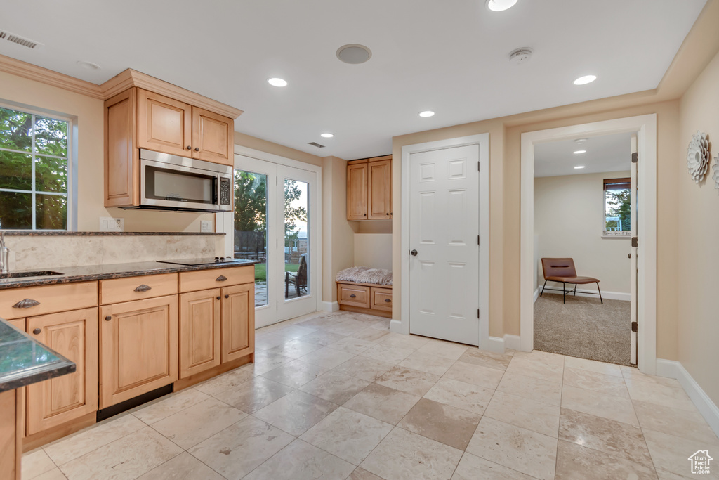 Kitchen with stainless steel microwave, recessed lighting, light brown cabinets, black electric cooktop, and dark stone countertops