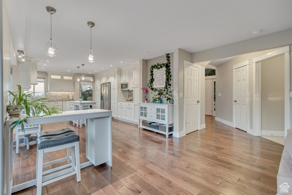 Kitchen with appliances with stainless steel finishes, a kitchen breakfast bar, light countertops, light wood-type flooring, and recessed lighting