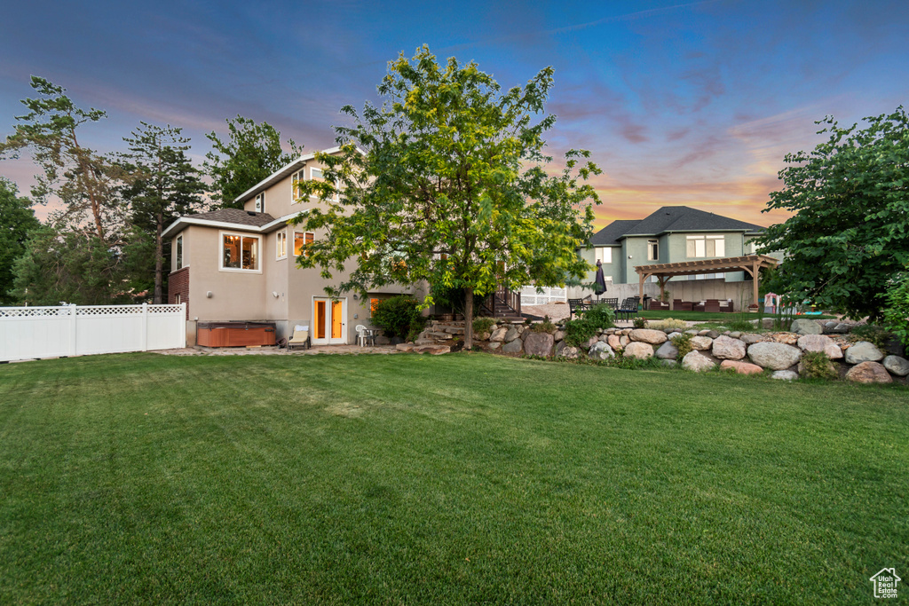 Back of property at dusk with a hot tub, a pergola, stucco siding, and a patio area