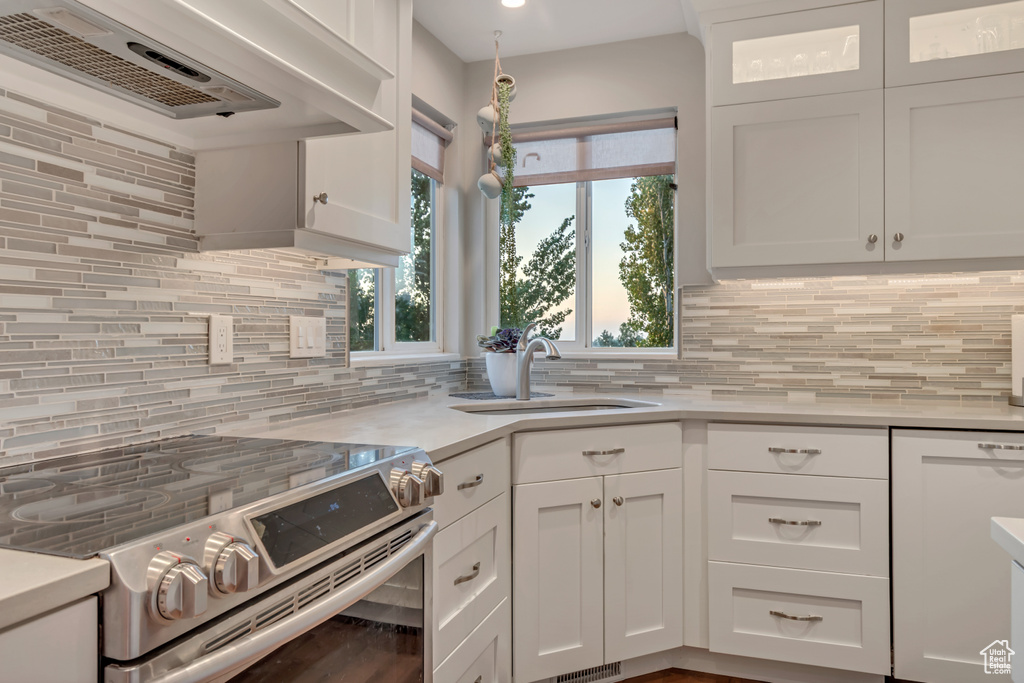 Kitchen featuring electric stove, backsplash, dishwasher, white cabinets, and light countertops