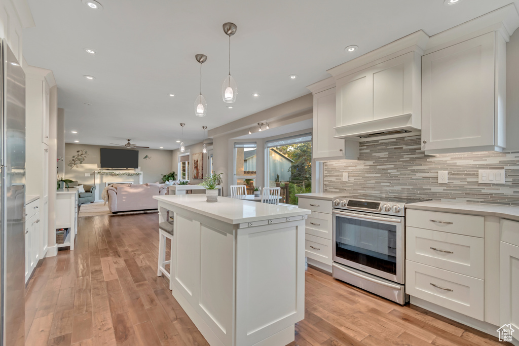 Kitchen with stainless steel electric stove, open floor plan, a kitchen island, backsplash, and light countertops