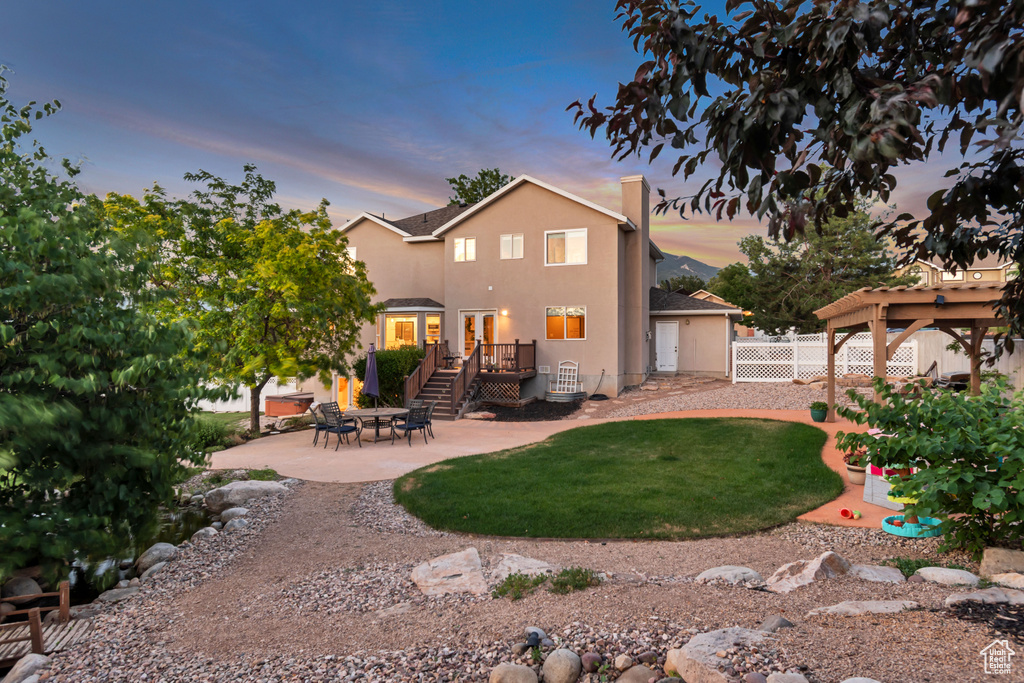 Back of house at dusk featuring a patio area, stucco siding, and a deck