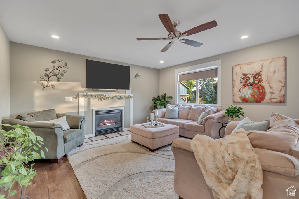 Living room with a glass covered fireplace, light wood-style floors, recessed lighting, and ceiling fan