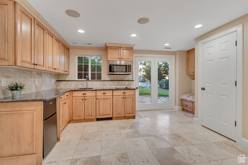 Kitchen with stainless steel microwave, backsplash, dark stone counters, recessed lighting, and light brown cabinetry