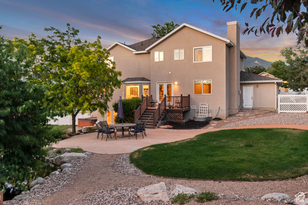 Rear view of house featuring a wooden deck, french doors, a patio area, a lawn, and a chimney